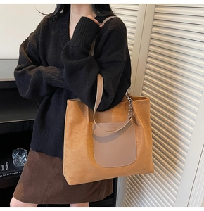 Detailed view of large brown tote bag featuring front leather pocket and metal chain strap