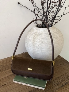 Deep brown retro underarm bag with vintage texture on wood surface and artistic decor