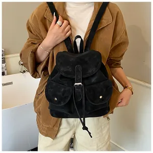 Detail of a large black suede backpack featuring a drawstring and flap buckle closure