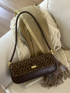 Brown leather baguette bag with leopard print flap and gold buckle on a soft blanket