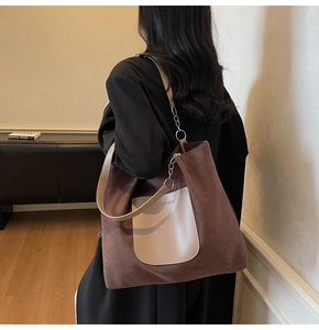 Detail of a large brown suede tote bag with chain strap worn over a black blazer