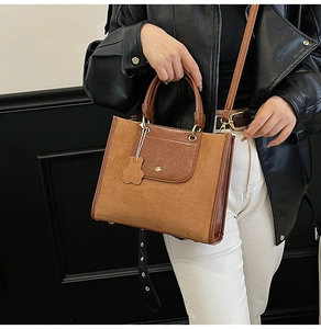 Close-up of brown suede and leather tote bag with floral charm and magnetic closure