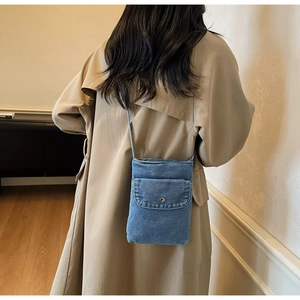 Detail of blue denim mini crossbody phone bag with metal snap button and distressed edges