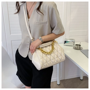 Close-up of cream shell handbag featuring quilted patterns and dual chain straps