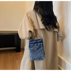 Detail shot of washed denim crossbody phone bag with metal button on a trench coat