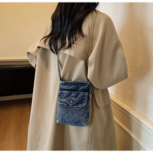 Detail of a mini washed denim crossbody bag on a khaki trench coat model back view