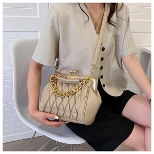 Detail of beige quilted shoulder bag featuring gold chain and retro clasp on a model