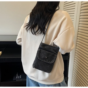 Detail of a dark gray denim crossbody phone bag worn by a model in a minimalist setting