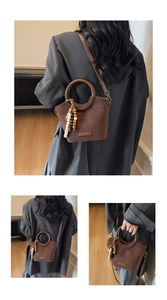 Detail of dark brown matte bucket bag featuring round handles and beaded fringe tassel