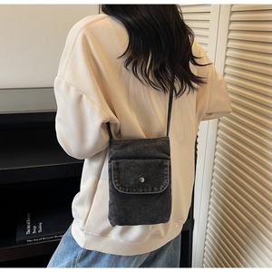 Detail of dark denim mini crossbody bag with metal snap button worn over casual beige hoodie