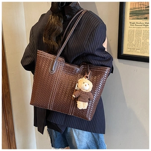 Detail of dark brown woven tote bag featuring white stitching and plush bear charm