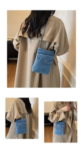 Detail of washed denim crossbody phone bag with metal button and textured fabric surface