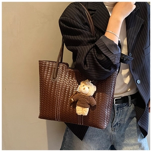 Détail d'un cabas tressé marron foncé avec un charmant ours en peluche attaché