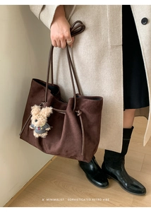 Detail of dark brown suede tote bag featuring slim leather handles and a plush bear charm