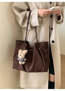 Detail of dark brown faux suede tote bag with drawstring knot and bear charm on beige coat