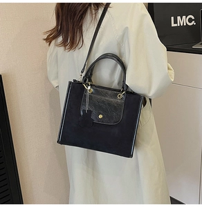 Detail of black suede and leather tote bag featuring golden hardware and bear pendant charm