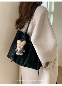 Detail of minimalist black suede tote bag with plush bear charm on beige wool coat