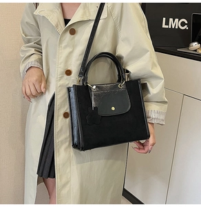 Detail of black tote bag with matte and glossy leather textures and gold hardware buckle
