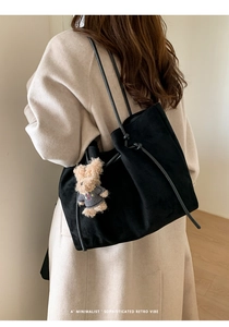 Close-up of black suede tote bag with a cute plush bear pendant on a shoulder strap