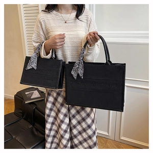 Detail of black vintage tote bag featuring embossed logo and decorative silk scarf handles