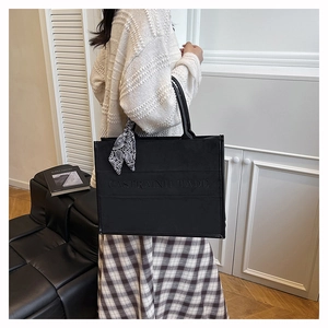 Detail of a black leather tote bag with embossed logo and decorative silk scarf accessory