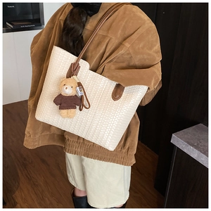 Détail d'un sac cabas tissé beige avec des bretelles en cuir marron et un pendentif ours