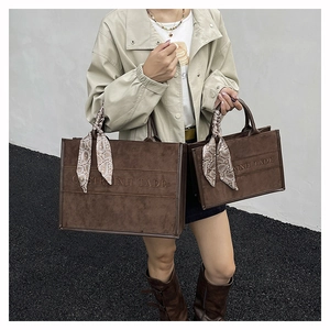 Detail of dark brown suede tote bags in two sizes featuring embossed text and paisley scarf