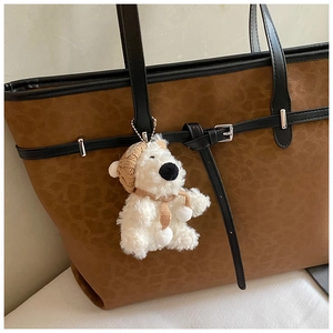 Close-up of white plush bear keychain charm with knit hat on a leopard print tote bag
