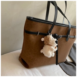 Detail of leopard print tote bag with black leather straps and plush puppy charm