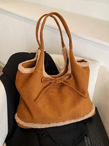Brown suede tote bag with faux shearling trim and bow detail on a white chair
