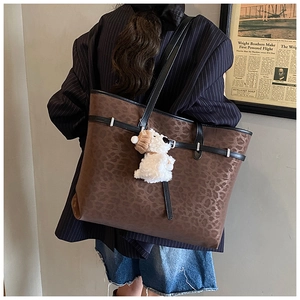 Detail of vintage leopard print tote bag with black straps and white plush dog charm