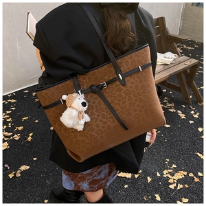 Detail of vintage leopard print tote bag with buckle and plush bear charm outdoors