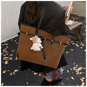 Detail of leopard print tote bag with plush puppy pendant in an autumn outdoor setting