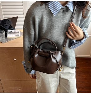 Detail of dark brown bucket bag with side drawstrings and gold metallic ball accents
