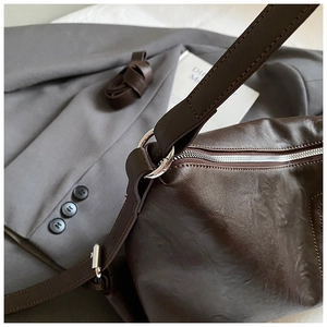 Detailed close-up of dark brown wrinkled leather texture and silver hardware on a tote bag