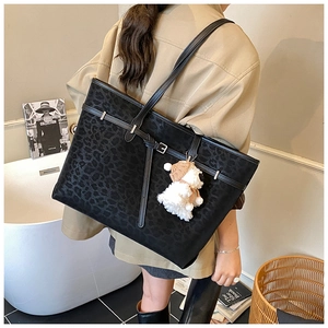 Detail of black leopard embossed tote bag with decorative strap and plush charm