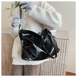 Detail of black glossy faux leather tote bag with dual handles and adjustable strap