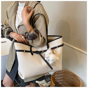 Detail of cream tote bag featuring black trim, buckle decor, and plush dog charm
