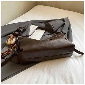 Detail of dark brown leather tote bag with soft texture and plush puppy charm accessory