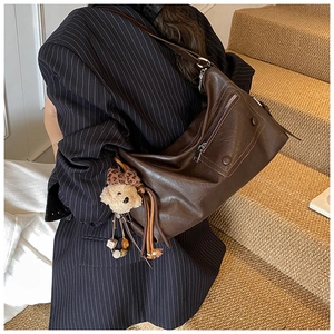 Detail of dark brown leather tote bag with vintage texture and bear charm