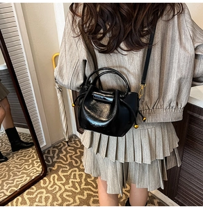 Detail of black glossy bucket bag featuring drawstring texture and gold sphere accents