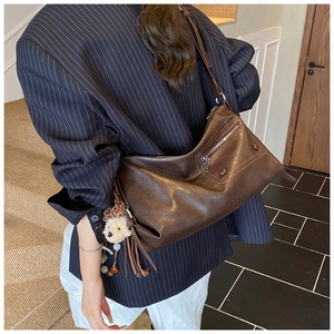 Detail of dark brown leather tote bag with stylish tassels and a bear charm accessory
