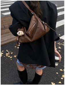 Brown leather tote with silver zipper detail and cute plush puppy charm on a street backdrop