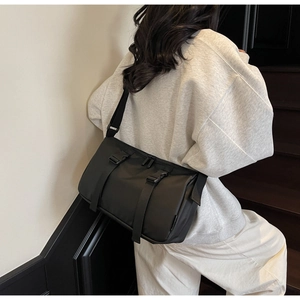 Model view of a black nylon crossbody bag with buckle straps and adjustable shoulder strap