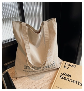 Close-up of beige canvas tote bag with text embroidery on minimalist marble surface