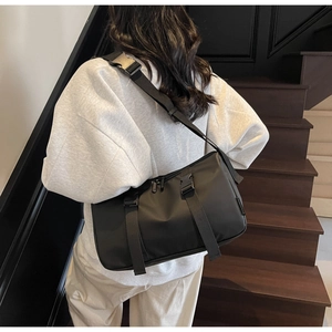 Detail of black nylon crossbody bag with dual buckles on adjustable straps shown on a model