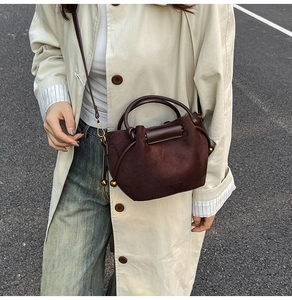Detail of dark brown suede bucket bag worn crossbody against a city street backdrop