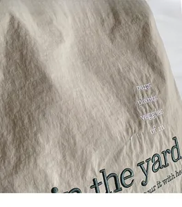 Close-up of beige canvas fabric with soft texture and green embroidered lettering detail