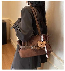 Detail view of large dark brown suede tote bag with decorative buckle and plush bear charm
