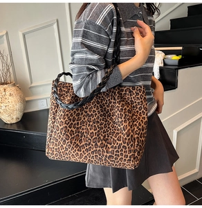 Detail of leopard print tote bag with black leather woven handles shown on a model